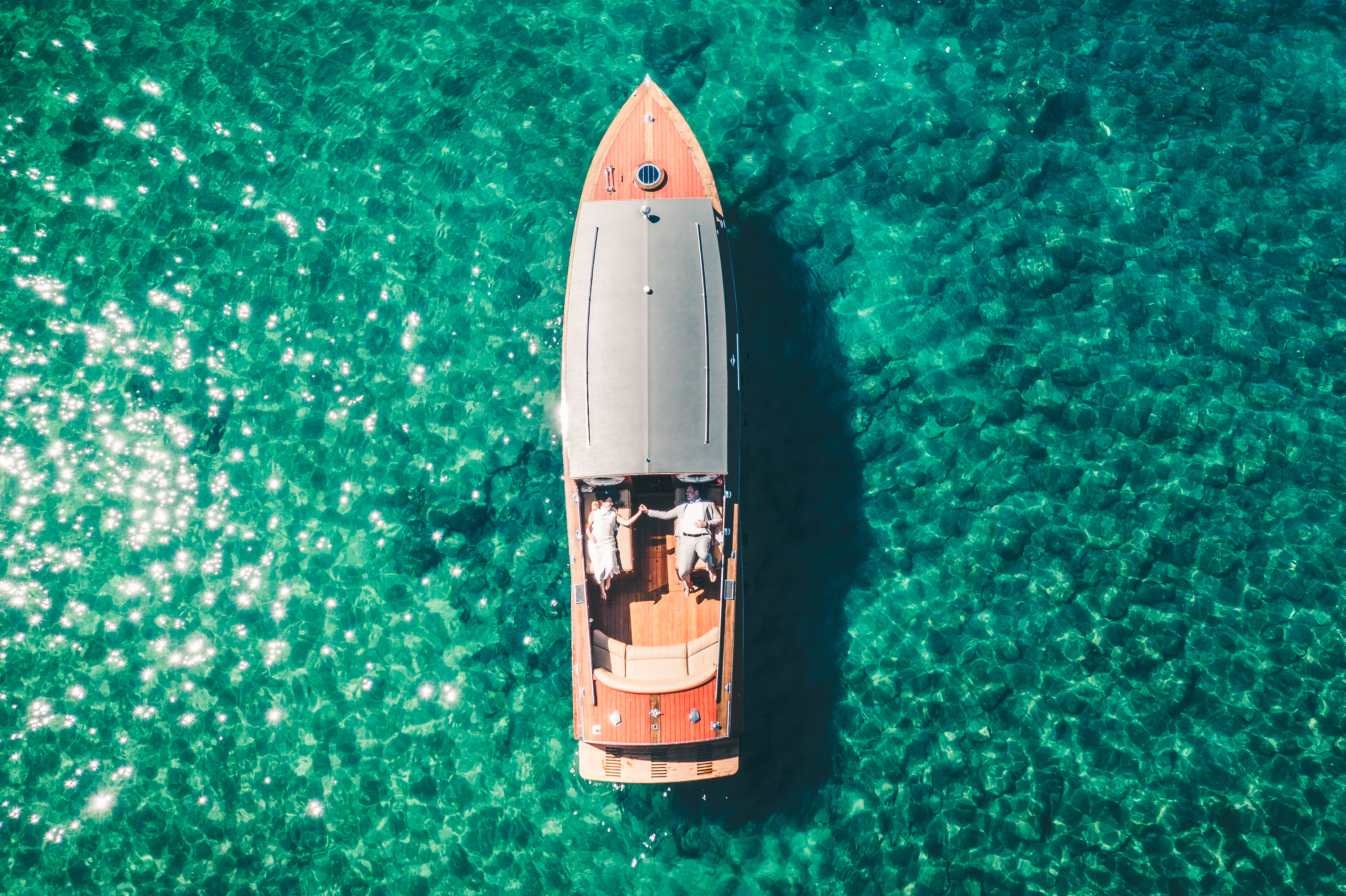 Aerial drone view of a wedding couple on a classic wooden boat surrounded by turquoise water