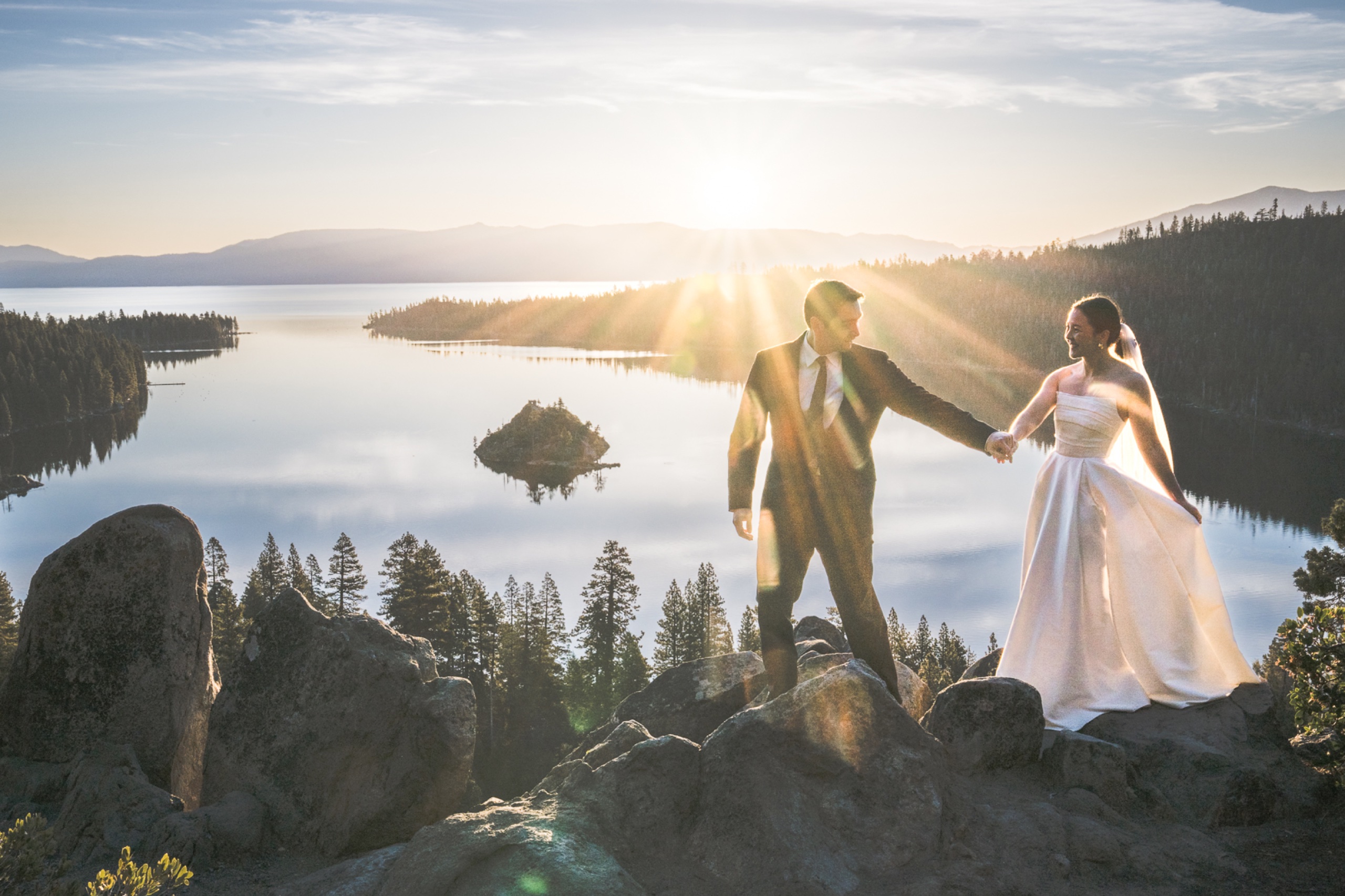 Couple standing on boulders above Emerald Bay at Lake Tahoe, California during a brilliant sunrise with star-burst light