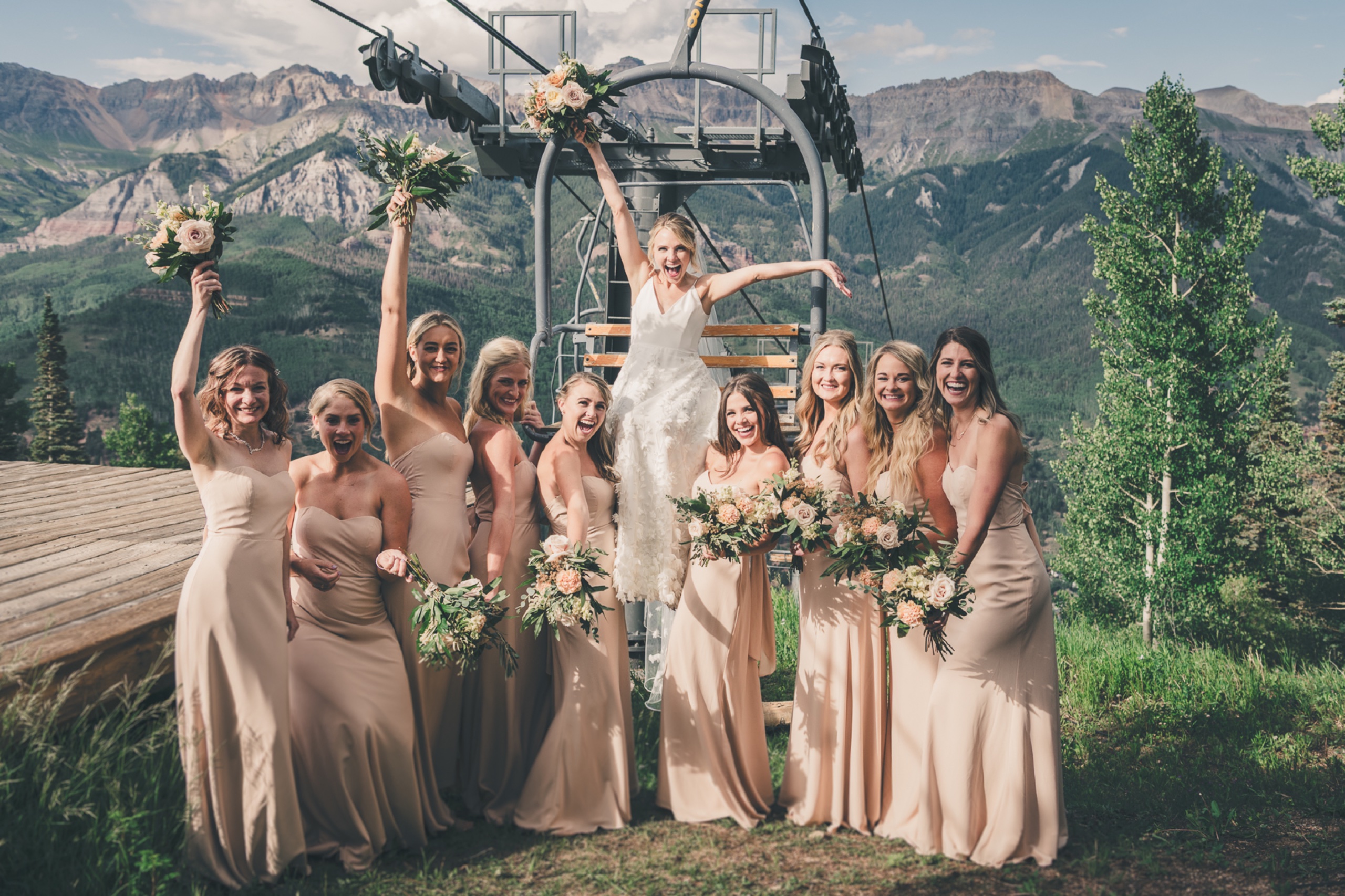 Bride jumping from a ski lift chair surrounded by her laughing bridesmaids against Telluride mountain scenery