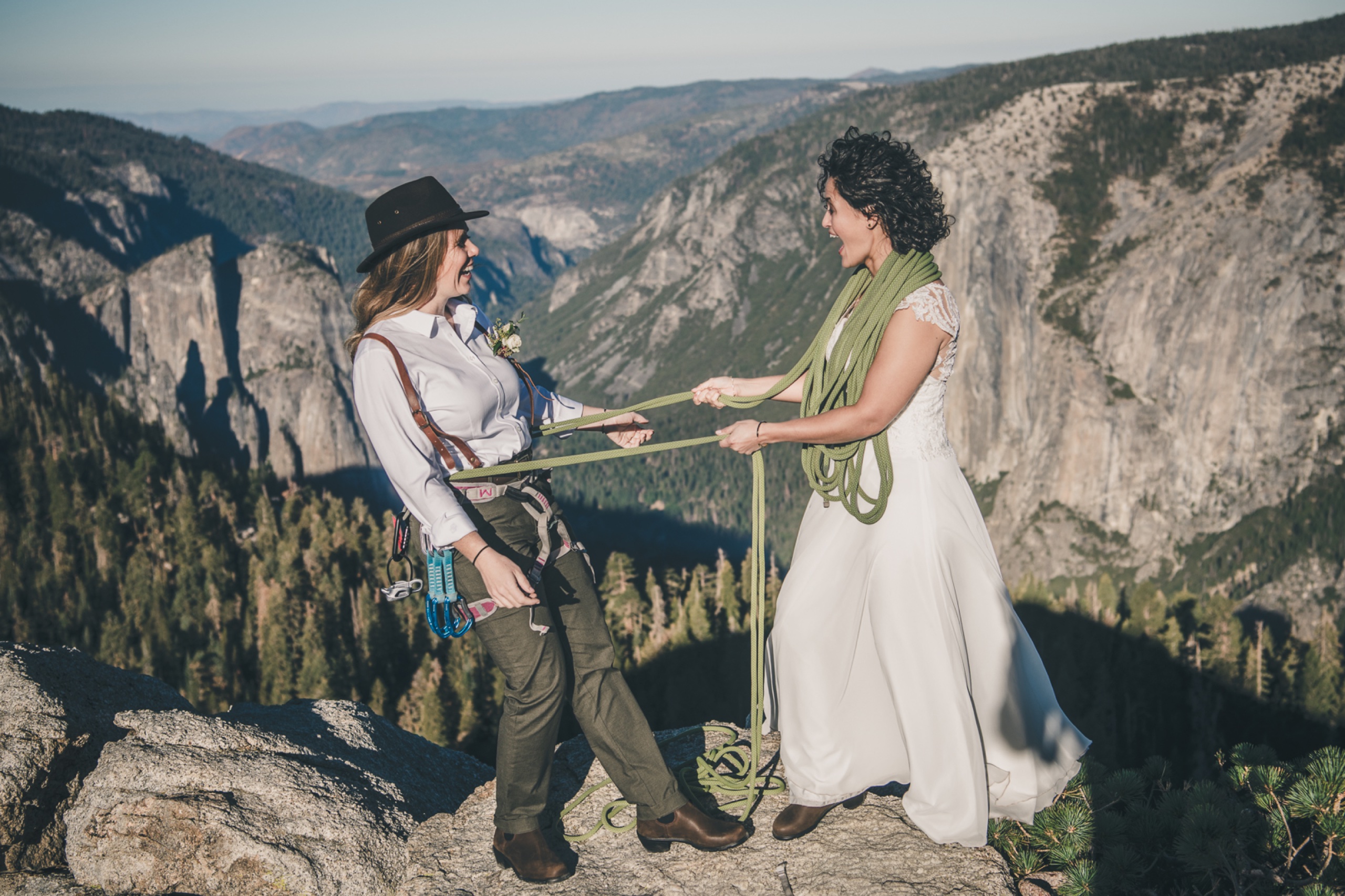 Two brides exchanging a meaningful moment with climbing rope on a cliff overlooking Yosemite Valley