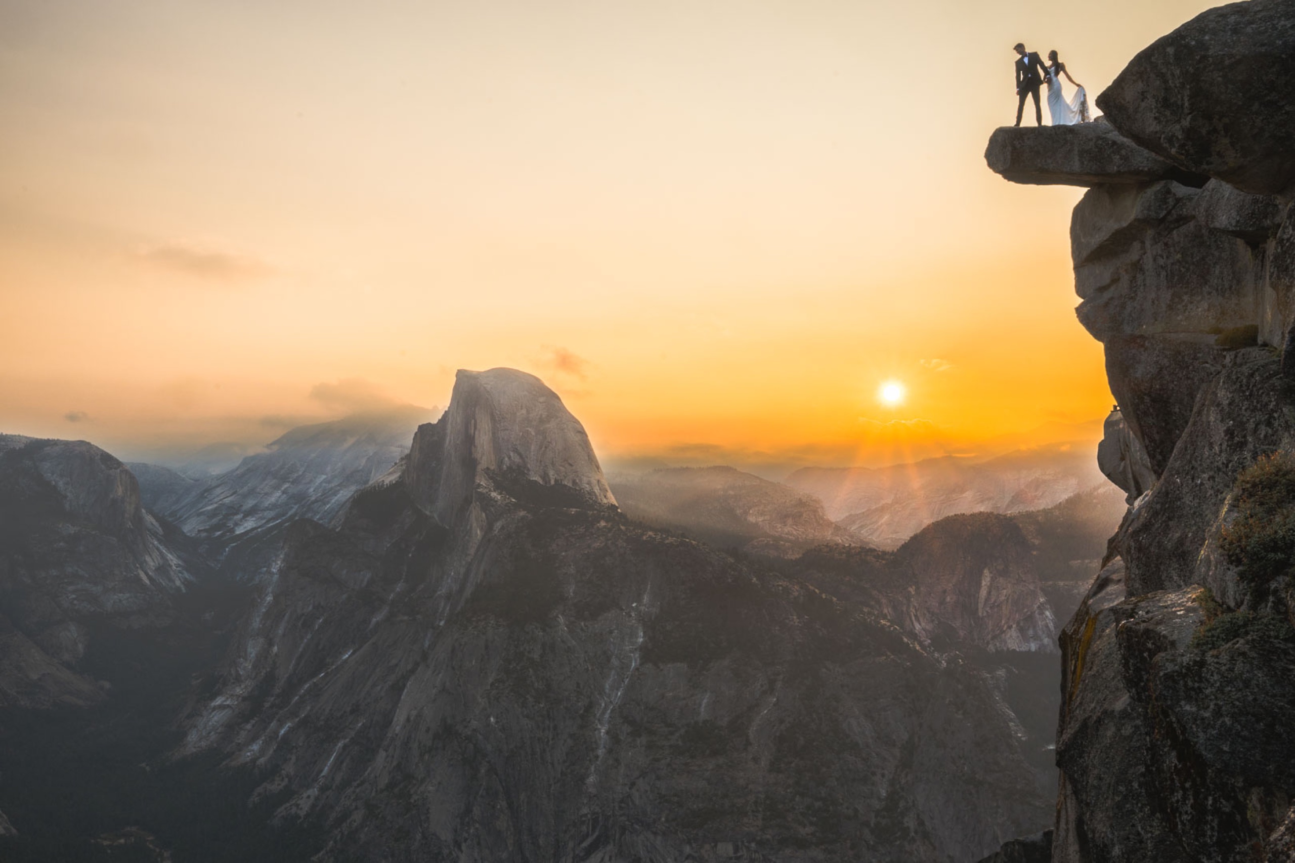 Silhouetted wedding couple standing on Glacier Point with Half Dome and a fiery Yosemite sunset stretching behind them