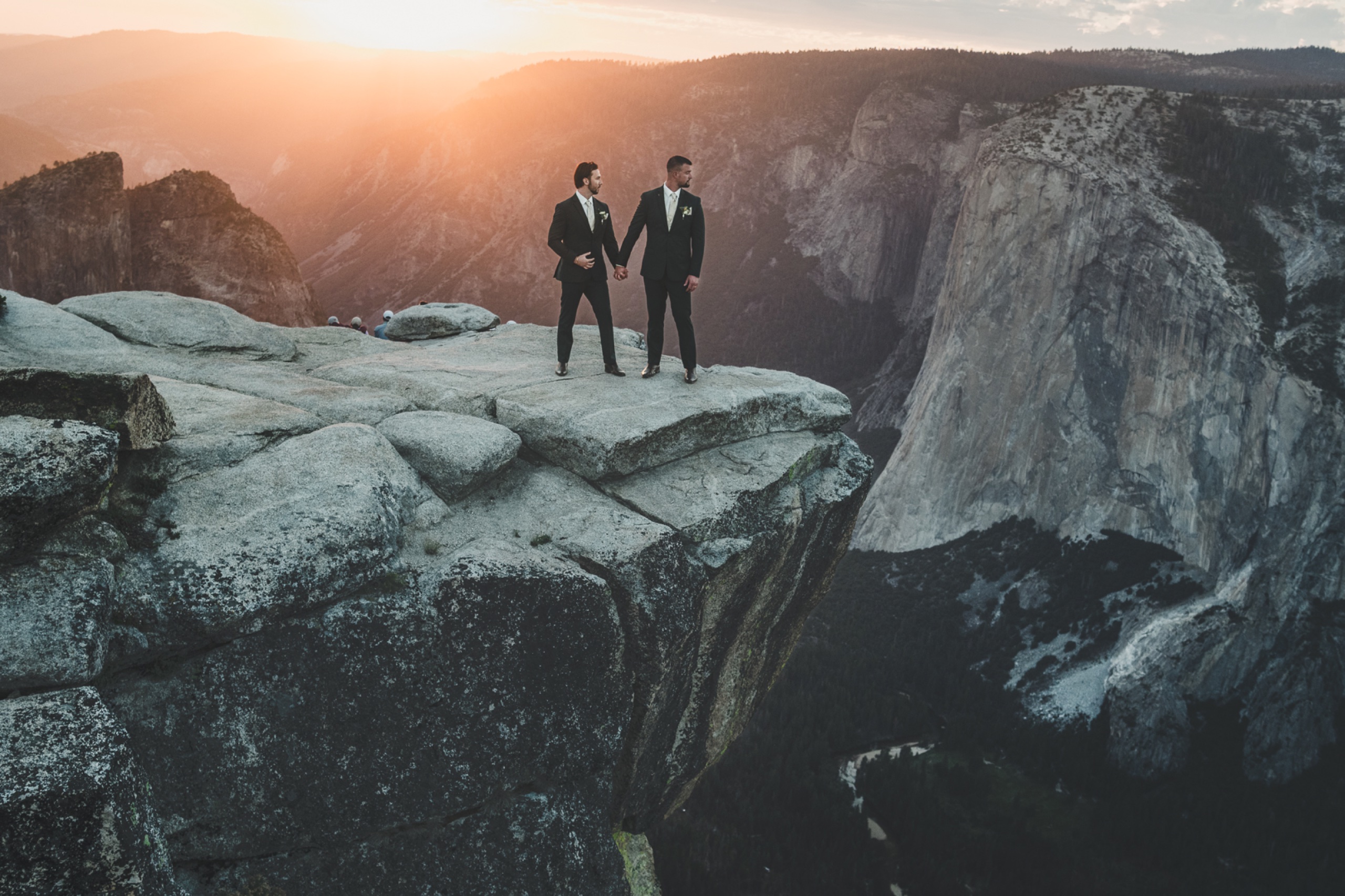 Same-sex couple holding hands on the edge of Taft Point in Yosemite with El Capitan glowing in the sunset behind them
